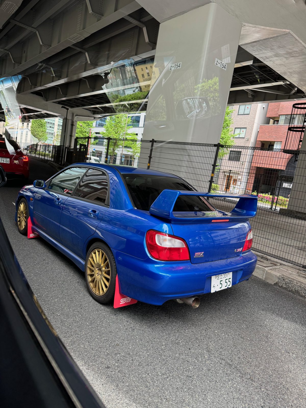 Blue Subaru Impreza WRX STI with gold wheels parked under an expressway in Tokyo